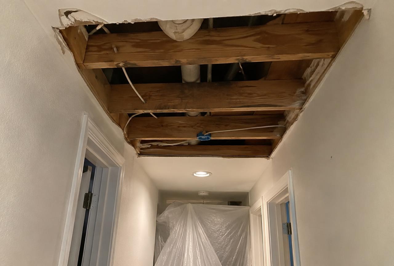 Water-damaged ceiling drywall cut out with joists exposed during repair in a Concord NC home